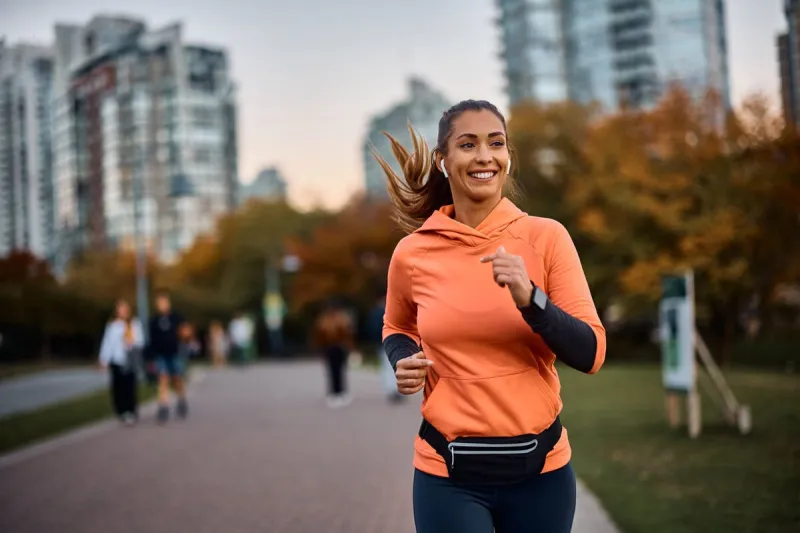 young happy athletic woman listening music on earphones while jogging in the park