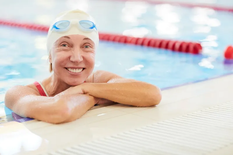 closeup portrait of happy senior woman in swimming pool, leaning on border and looking at camera, copy space