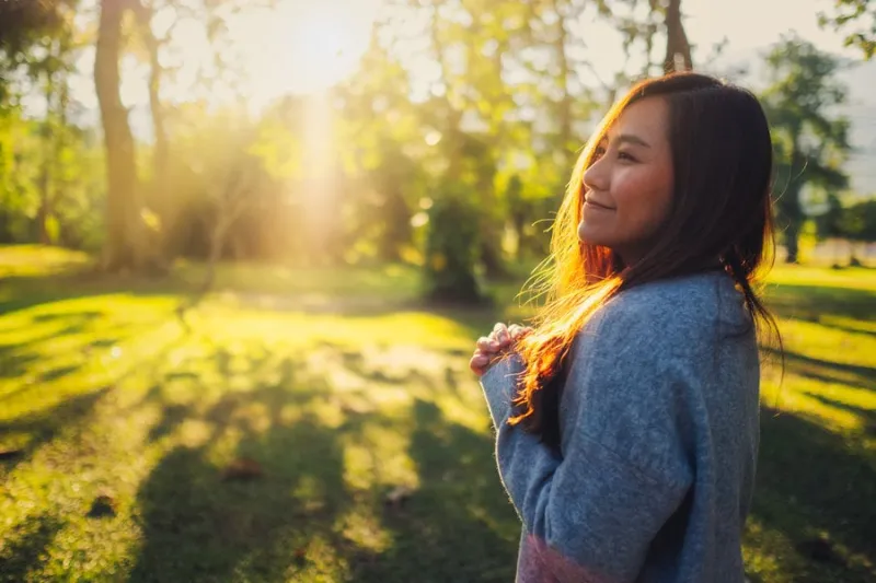 portrait image of a beautiful asian woman standing among nature in the park before sunset