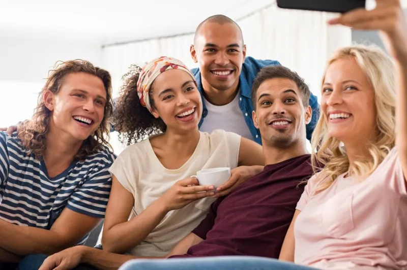 group of multiethnic friends taking selfie at home smiling men and young women with smart phone taking selfie while sitting on couch group of funny boys and happy girls taking photo with smartphone