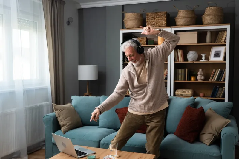 happy senior old grandfather man in wireless headphones dancing, singing at home, choosing favorite energetic disco music in mobile application, entertaining indoors retired people relax activities