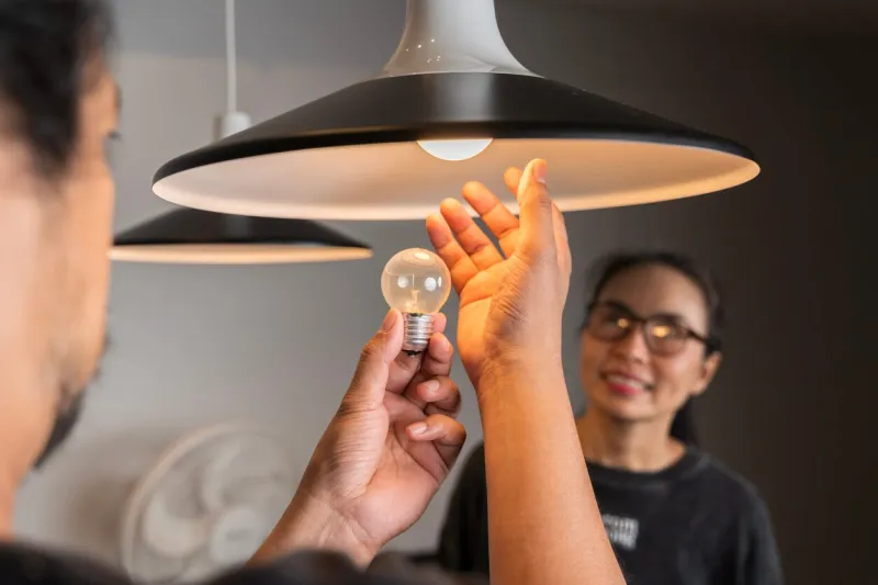 male hands compare an incandescent light bulb and a led lamp changing light bulb man installs light fixture in new home a man changes a light bulb in an apartment by himself