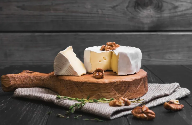 camembert cheese, walnuts, thyme, sacking on cutting board, cut slice camembert cheese, dark black wooden background