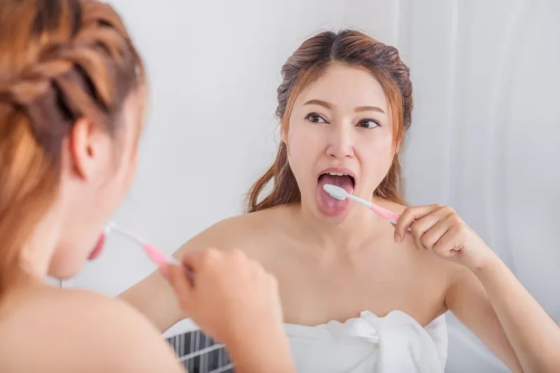 woman cleaning tongue using toothbrush with mirror in the bathroom