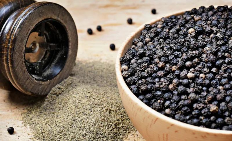 black peppercorns and milled pepper, arrangement in a wooden bowl close up shot of black pepper, cooking ingredient scene and wooden table top view