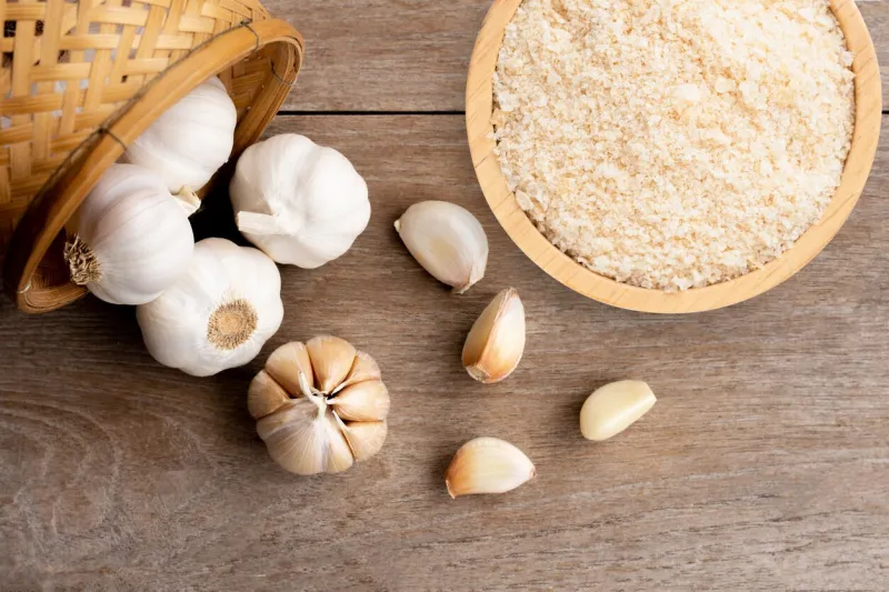 garlic powder in wooden bowl and bulb of garlic isolated on wooden table background top view flat lay