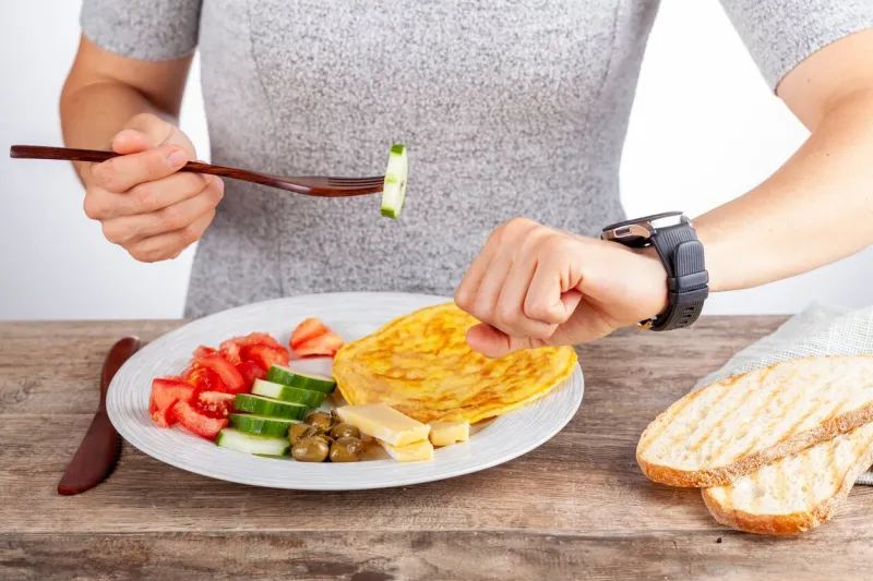 intermittent fasting concept with a woman sitting hungry in front of food and looking at her watch to make sure she breaks fast on the correct time a dietary modification for healthy lifestyle
