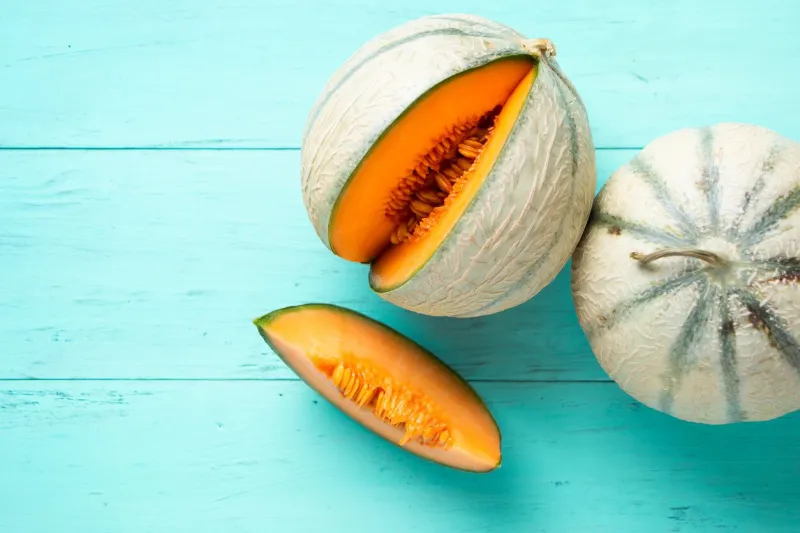 two cantaloupe melons and one slice on an aquamarine wooden planks top view