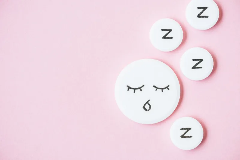 top view of sleeping pills with drawn face and z signs on pink