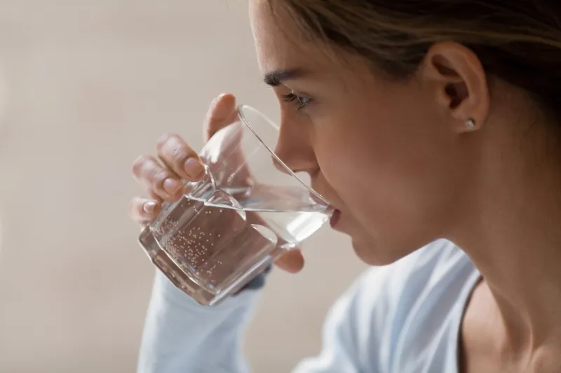 closeup profile portrait of woman drinking pure water from glass beautiful young brunette female feeling thirsty, making sip of water, taking her pills, medication healthy lifestyle idea concept