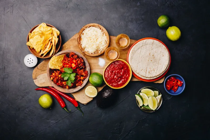 concept of mexican food (corn tortillas, nachos, salsa, avocado, limes, cheese, chili con carne) flat lay