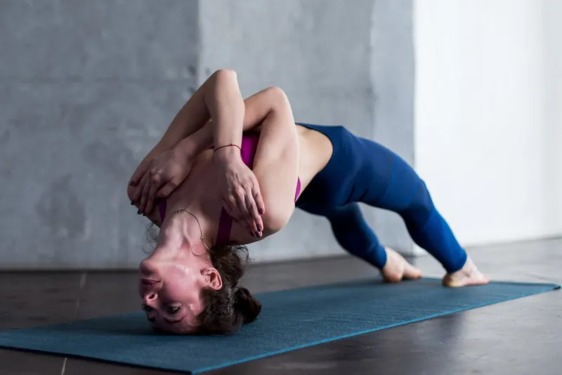 young caucasian female doing challenging headstand backbend yoga pose with her arms crossed on chest