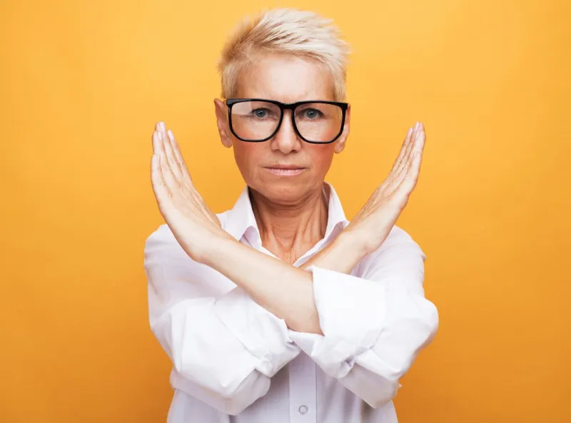 lifestyle, emotion and old people concept  senior woman with short gray hair wearing white shirt and glasses rejection expression crossing arms doing negative sign over yellow background