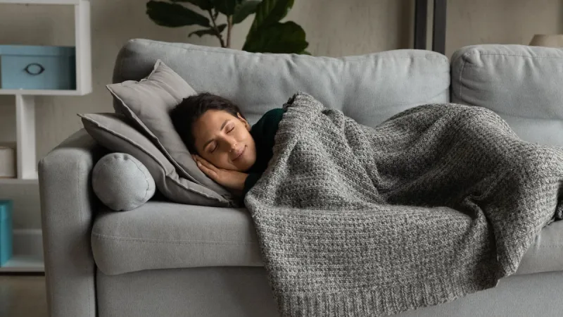 happy millennial caucasian woman lying under blanket on cozy couch at home sleeping or dreaming smiling calm young female relax rest on sofa in living room, relieve negative emotions daydreaming