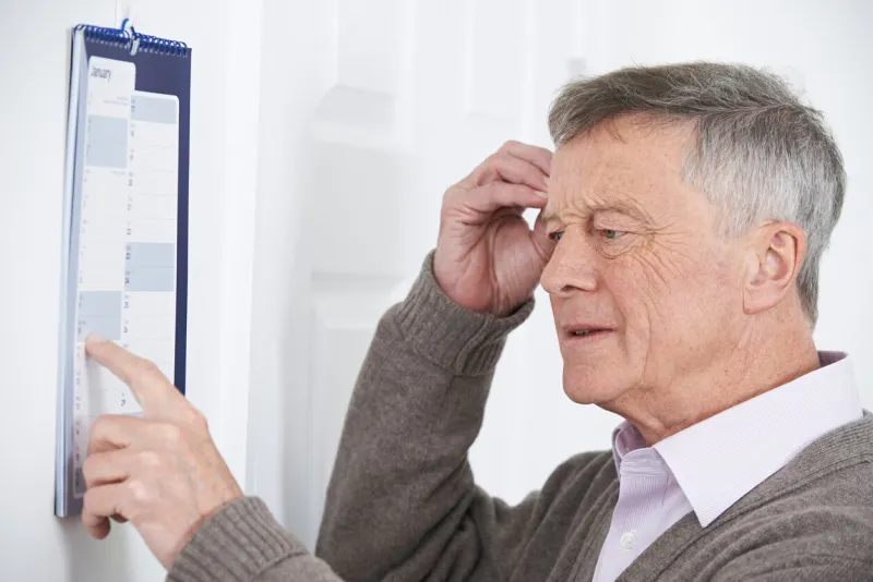 confused senior man with dementia looking at wall calendar