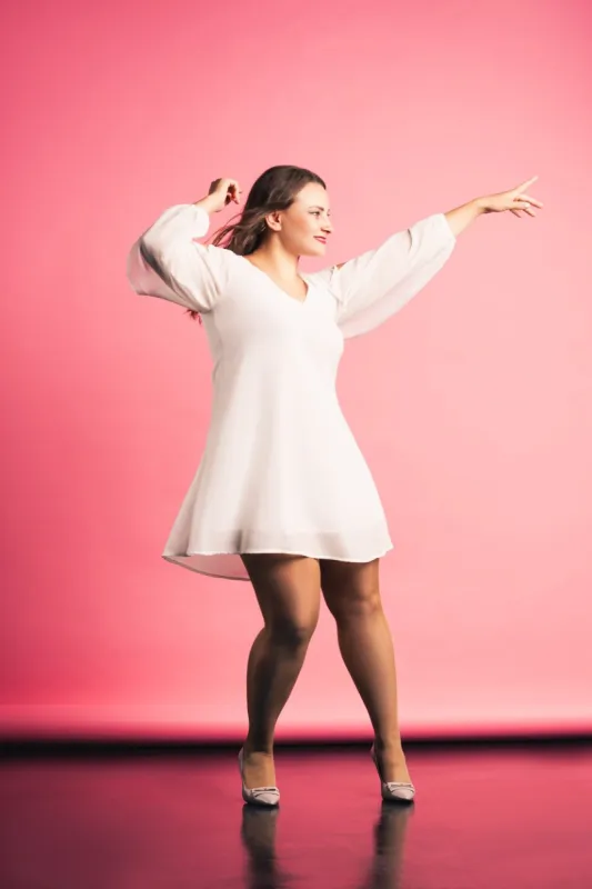 happy plus size fashion model in white dress dancing on pink background, body positive concept