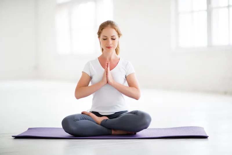 woman practicing yoga and meditating in lotus position at home