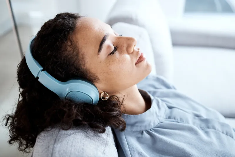 face, woman and headphones for listening to music for calm, peace and mindfulness on home couch young person on living room sofa listen to podcast, audio or motivation to relax or meditation profile