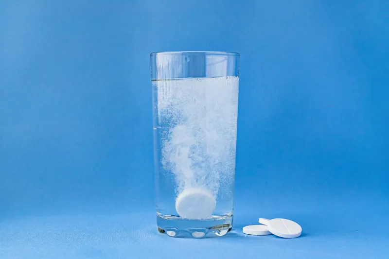 fizzy aspirin in a glass of water on a blue background vertical