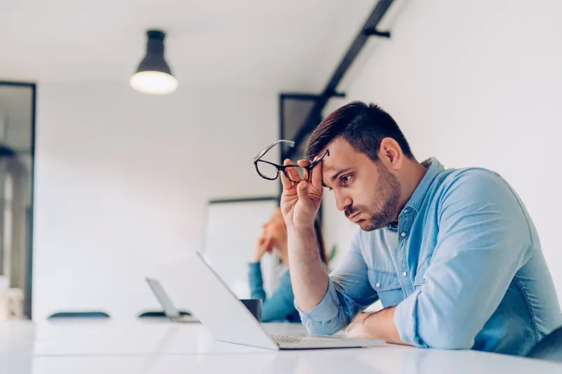 exhausted young businessman using laptop at work and sitting by the desk while