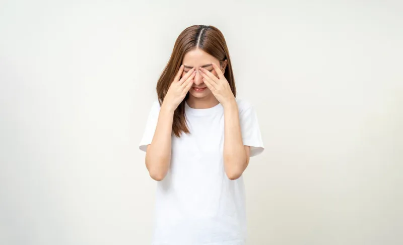 young asian beautiful woman hand rubbing eyes she's feeling depressed stress headache be tired from working standing on isolated white background she has health problems