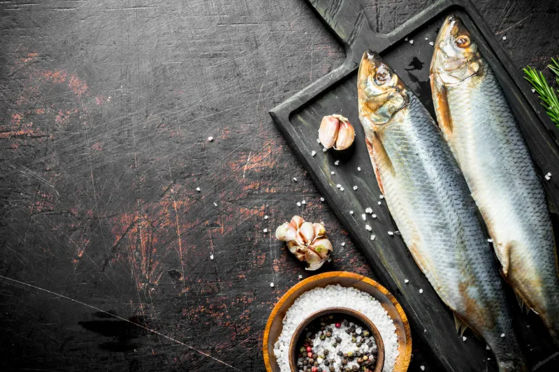 salted herring with garlic cloves and spices in bowl on dark rustic background