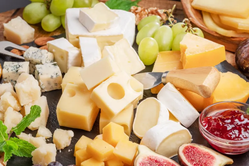 variety of sliced cheeses with fruits, mint, nuts and cheese cutting knives wonderful cheese background for your projects
