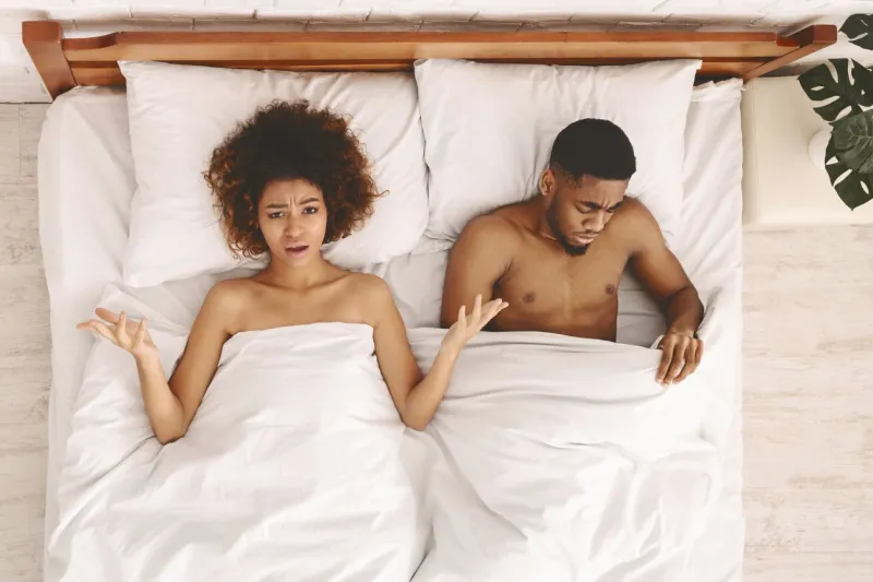 sex problem disappointed black unsatisfied woman lying in bed, sad man looking under blanket, top view