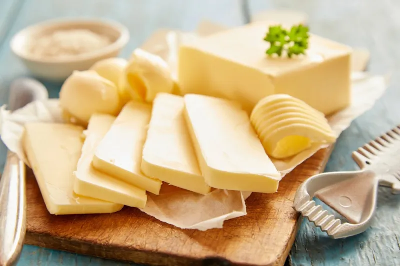 close up view of butter sliced on cutting board against blue wooden background
