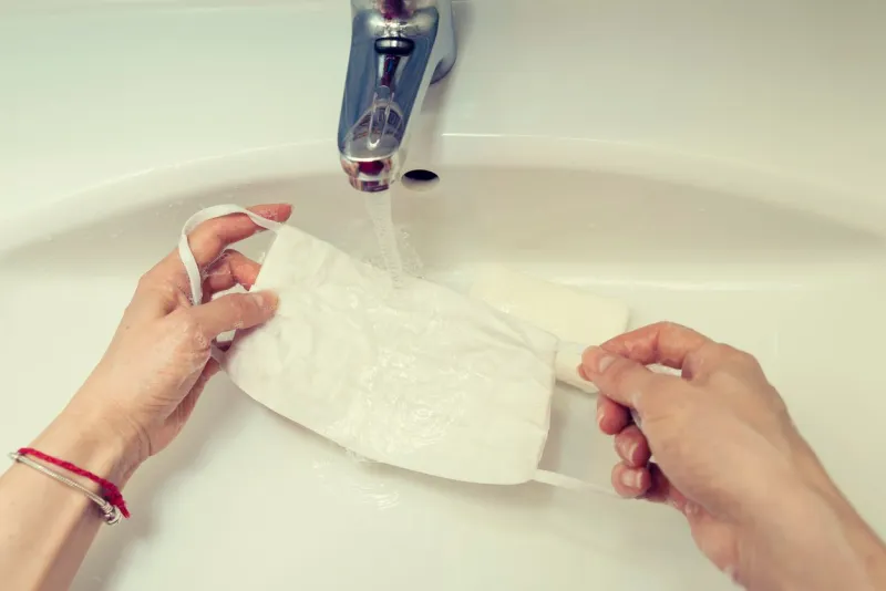 female caucasian hands in laundering handmade protective mask with soap and water on a sink selective focus
