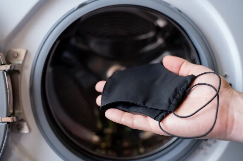 the hand of a man who is throwing a black mask into the washing machine