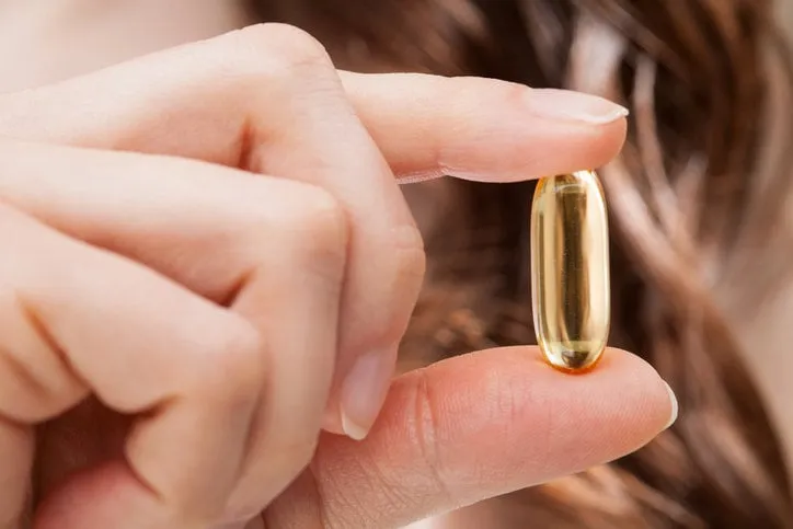closeup of woman hand showing omega-3 capsule for healthy hair, strong nails and shiny skin