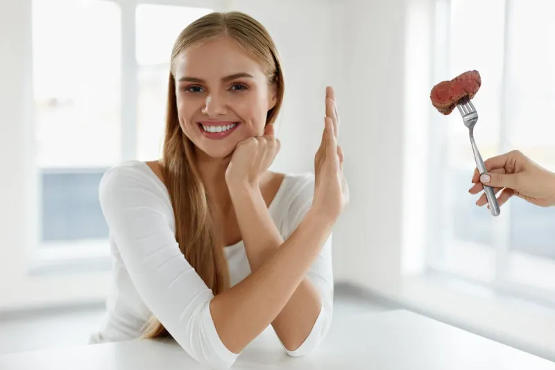 beautiful woman refuses to eat red meat female hand holding fork with piece of beef steak, proposing it to girl attractive female with stop hand sign vegetarian nutrition concept high resolution