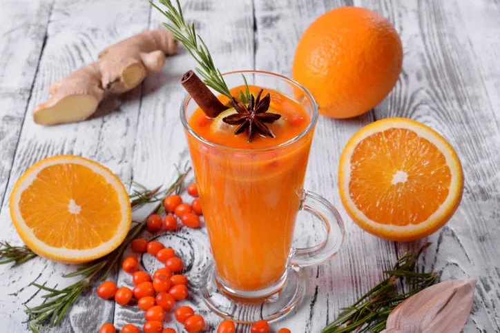 fruit punch with sea buckthorn berries, citrus and spices in a tall glass on white wooden table