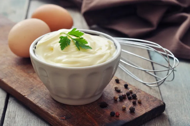 homemade mayonnaise in bowl with eggs and spice on wooden background