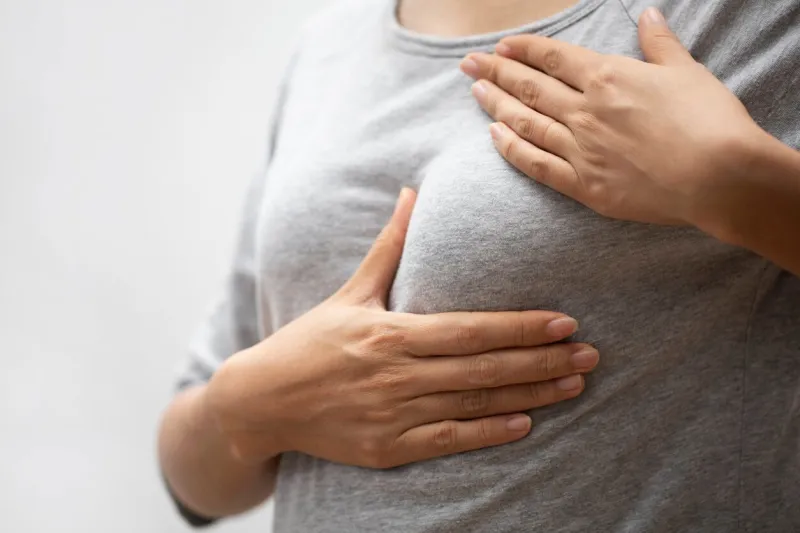 woman hand checking lumps on her breast for signs of breast cancer on gray background healthcare concept