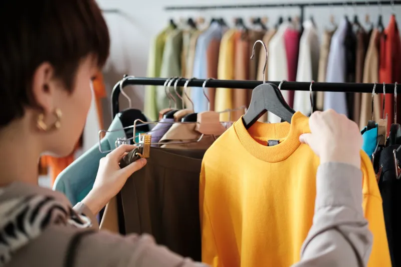 rear view of young woman looking at clothes on rack in her hands and choosing a new style for herself in the clothes store