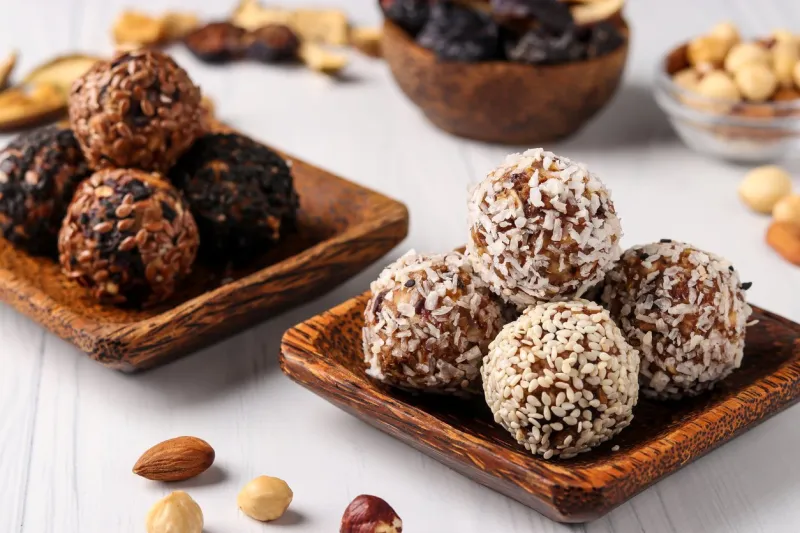 healthy energy balls of nuts, oatmeals and dried fruit with coconut, flax and sesame seeds on wooden coconut plates on a white background, horizontal orientation, closeup