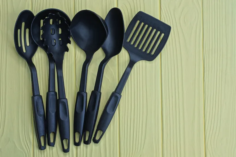 a set of six black plastic kitchen utensils lie on a yellow wooden table