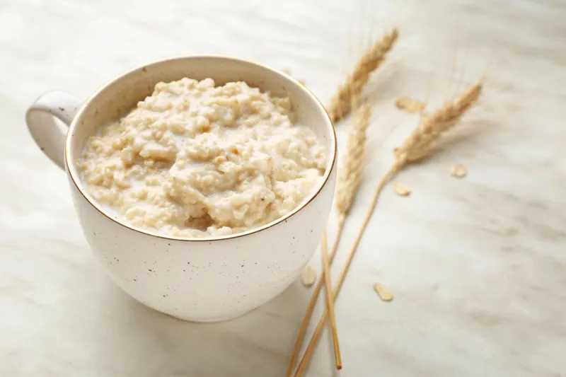 cup with tasty oatmeal on light table