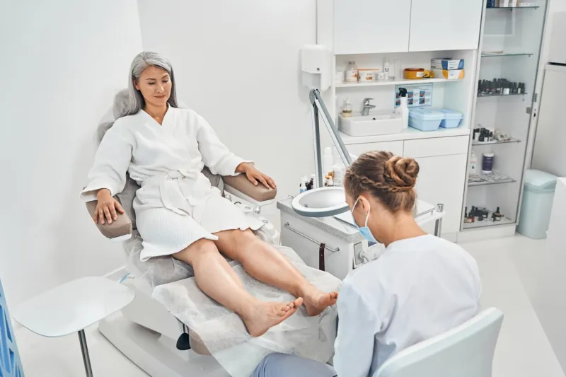 attentive nail master sitting at her workplace while doing professional medical pedicure