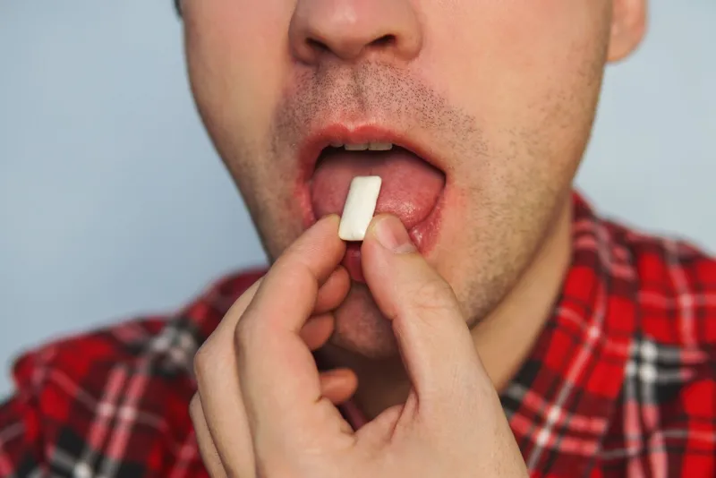 young funny guy with chewing gum fresh breath bad breath to quit smoking using the gum brush up brushing your teeth after meals with gum man puts his open mouth in white cushion gum closeup
