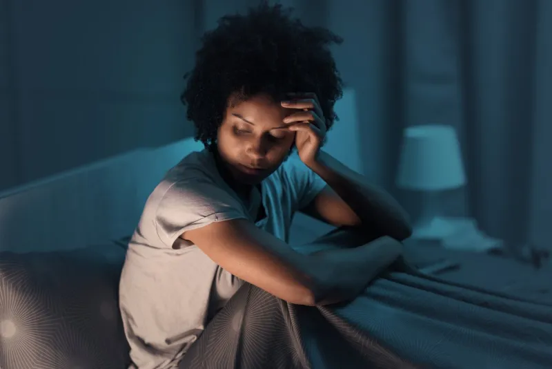 sleepless african american woman sitting in bed at night, she is stressed and unable to sleep