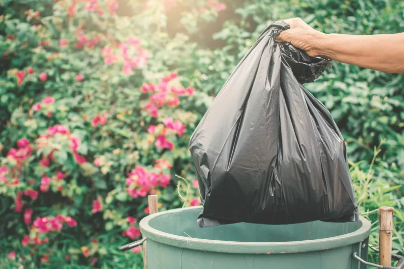 old hand holding plastic bag in to trash
