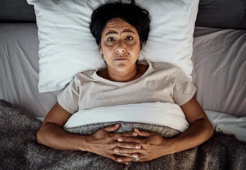 insomnia, portrait and senior woman in bed from above with menopause, anxiety or stress in her home top view, face and elderly female in a bedroom with depression, trauma or mental health crisis