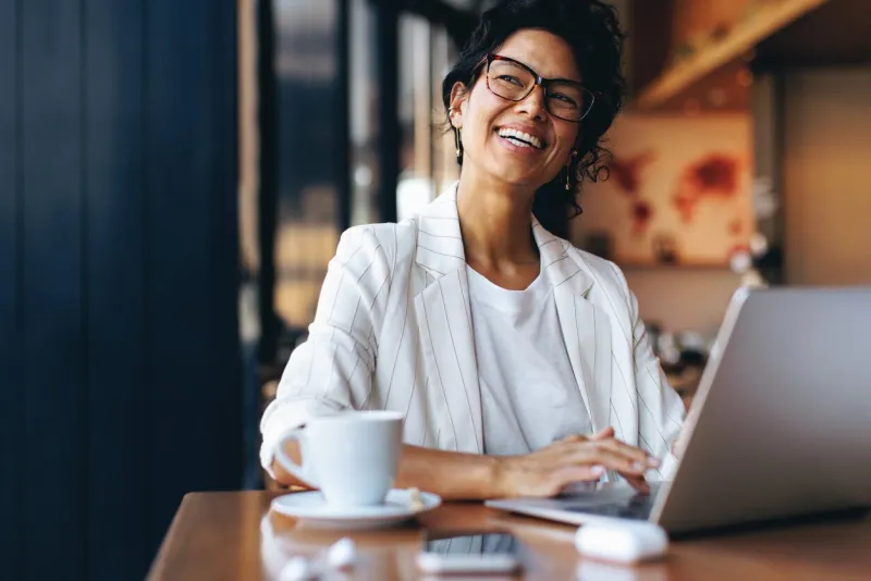 happy businesswoman working remotely on her laptop in a cozy cafe energized freelance worker using smartphone and enjoying her coffee