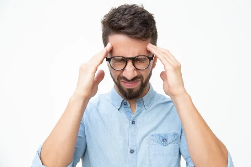 stressed man suffering from headache front view of young man in light blue shirt and eyeglasses suffering from headache and touching head on white background stress concept