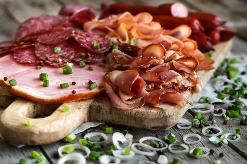 mix of meat appetizers - salami, ham, smoked turkey, sausages and prosciutto - on rustic wooden background