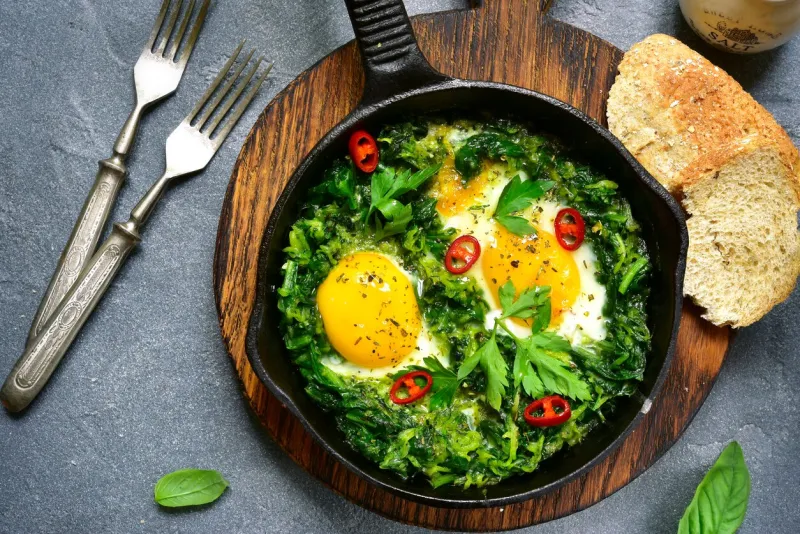 green shakshuka in a cast iron pan on a grey slate,stone or concrete backgroundtop view