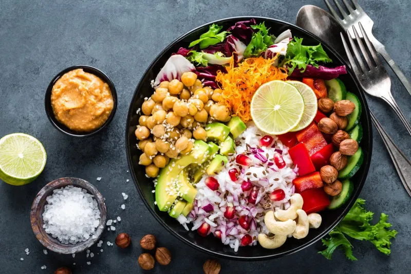 healthy vegetarian buddha bowl with fresh vegetable salad, rice, chickpea, avocado, sweet pepper, cucumber, carrot, pomegranate and nuts closeup